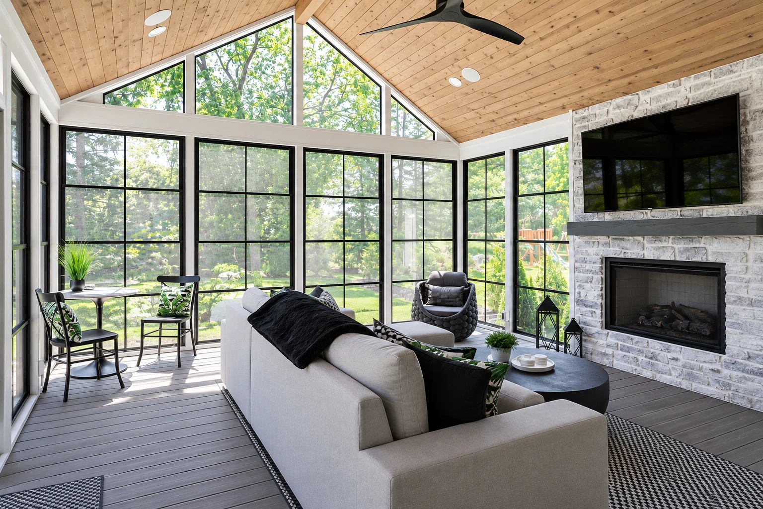 All-season sunroom with a vaulted wood ceiling, tall black-framed windows, a stone fireplace and lounge seating.
