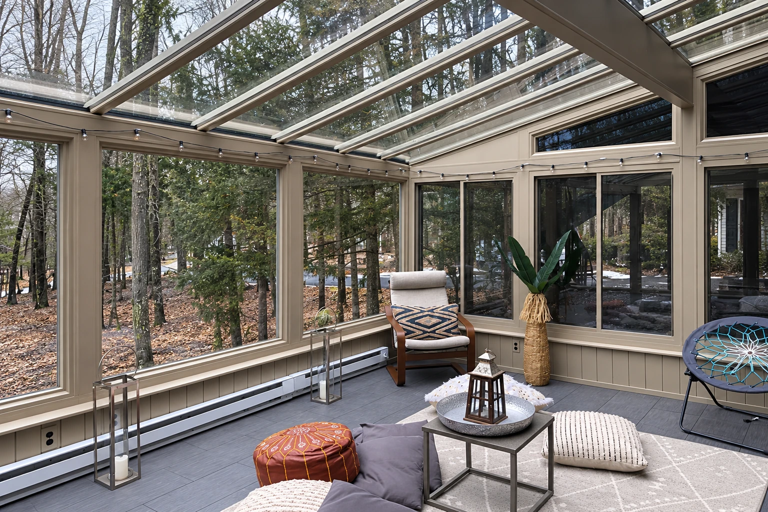 Four-season sunroom with a glass roof, beige-framed windows, and a wooded view.