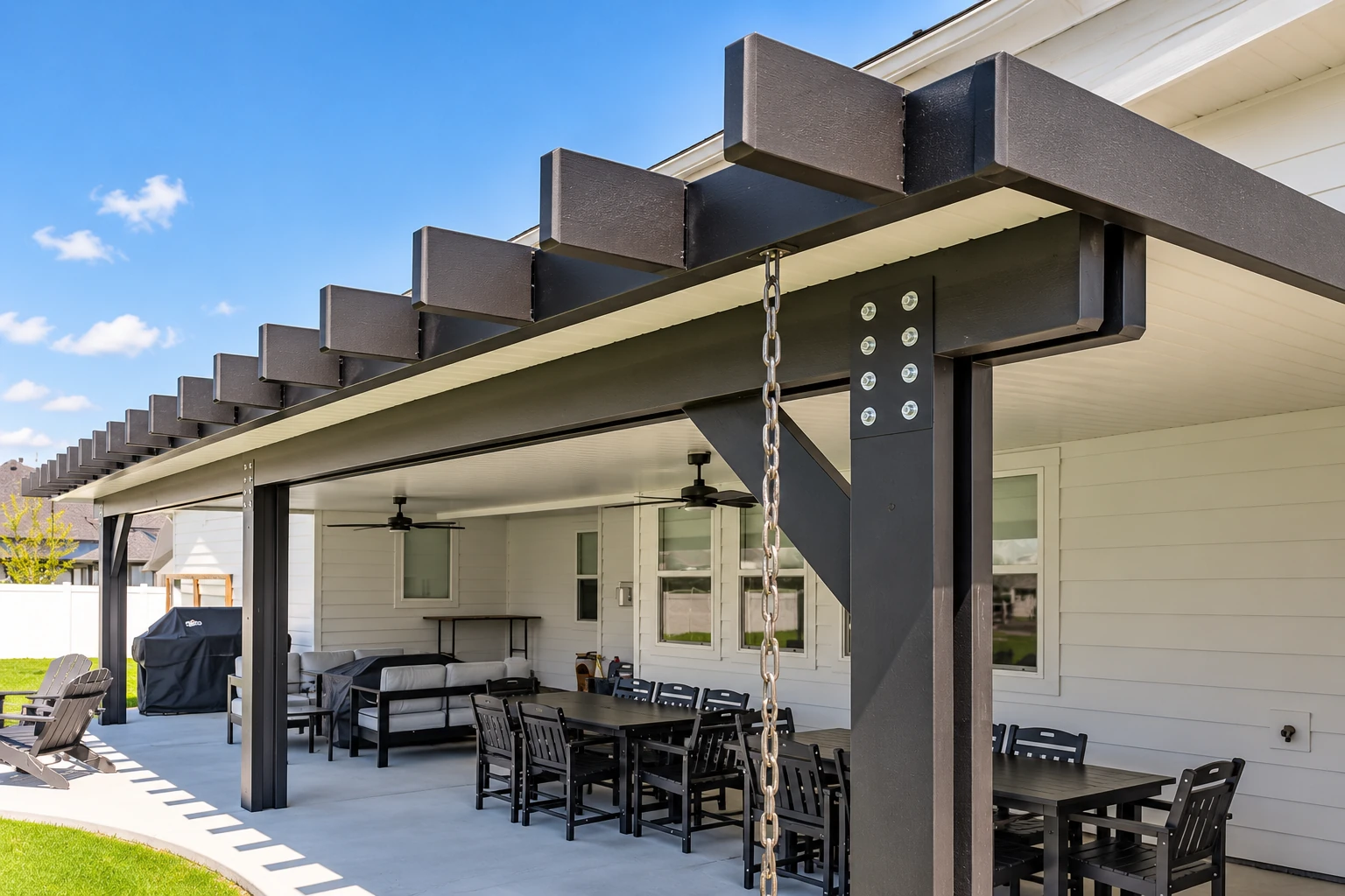 A covered patio features a dark pergola roof, sturdy posts and outdoor dining and lounge furniture.