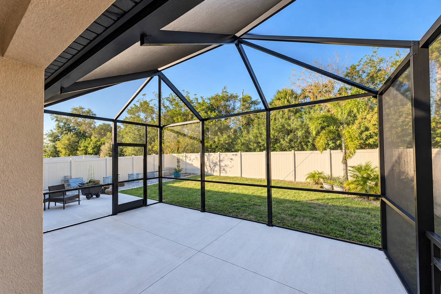 A screened patio enclosure with black framing and a peaked roof opens onto a fenced backyard.
