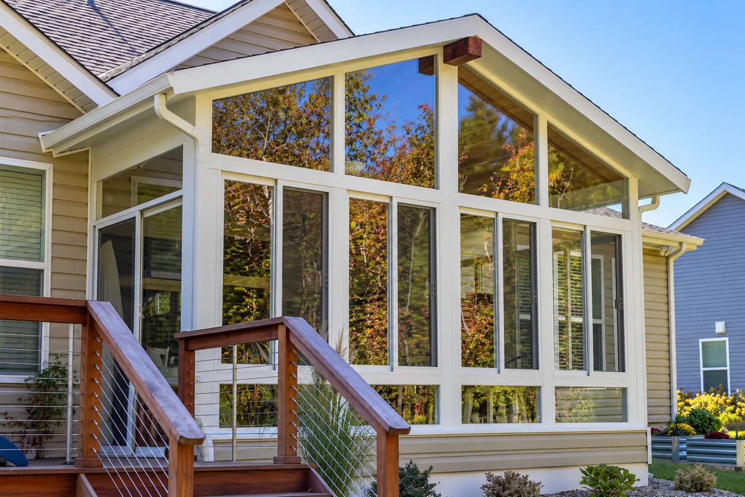 House sunroom addition with a steep gabled roof, tall white-framed windows and a wooden staircase.