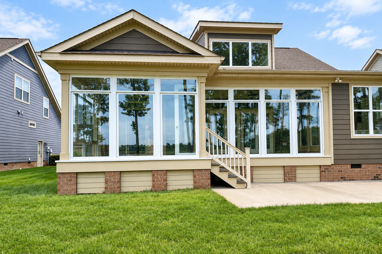 A wide, white-framed sunroom with floor-to-ceiling windows and a gabled roof spans the back of a house.