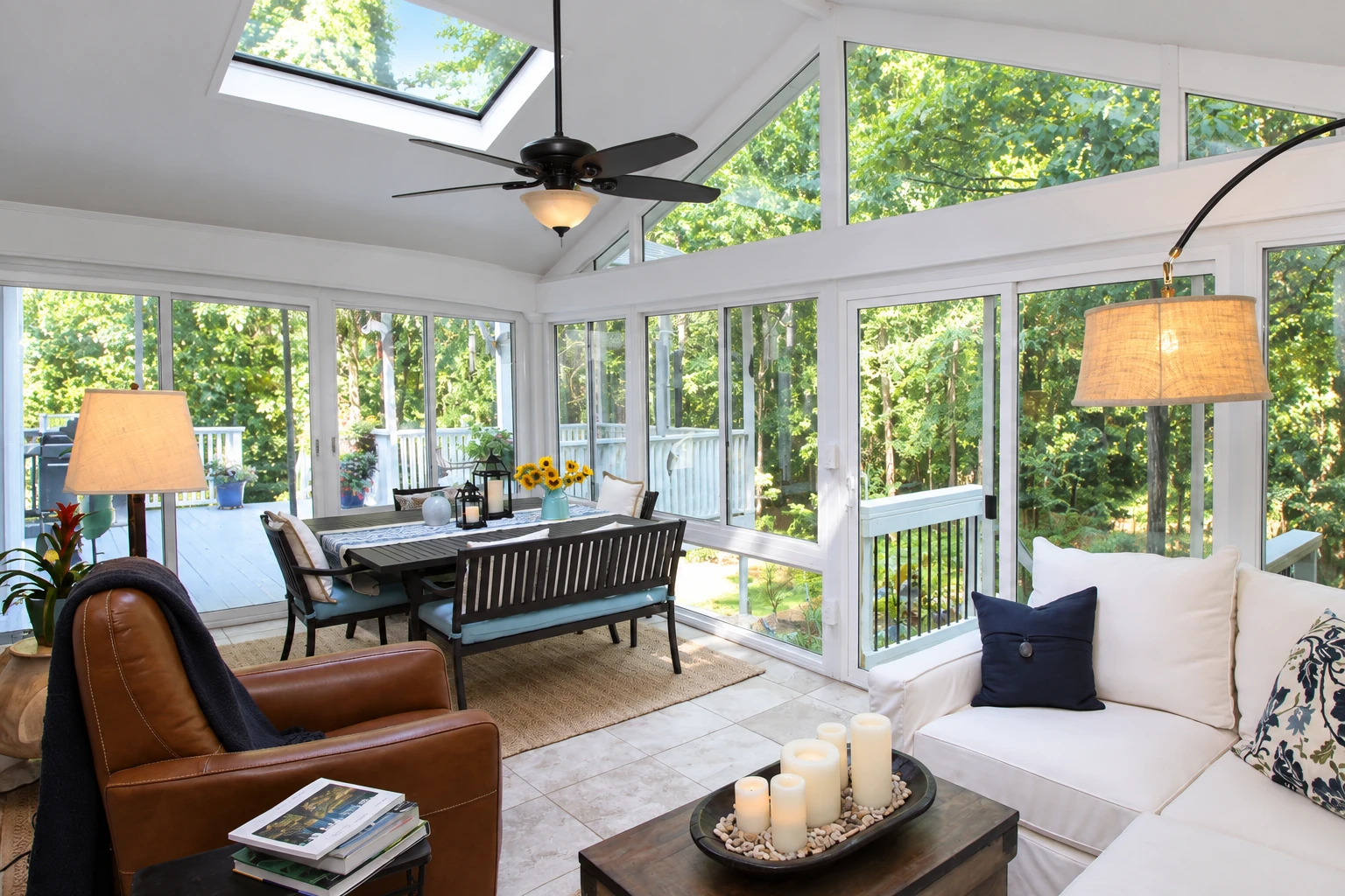 Bright vinyl sunroom with white frames, skylight, dining table and seating beside a wooded deck.